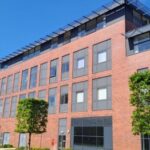 red brick building with grey windows and tree lined walkway